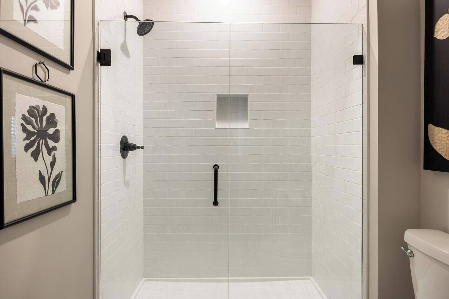 A shower with white tiled walls, a glass door, and a black handle.