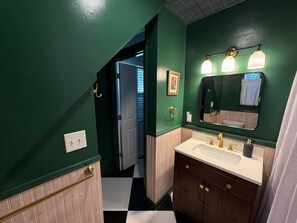 A bathroom with green walls, a white sink, and a mirror with three lights.