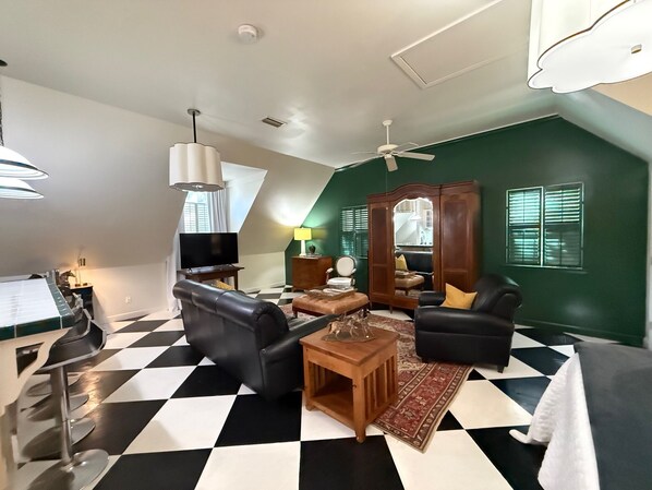 A living room with a checkered floor, a black leather sofa, a wooden coffee table, and a TV.