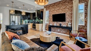 A modern living room with a sofa, coffee table, and TV against a brick wall. - NEW!  Sleek Rooftop Retreat - Sleeps 10 (Nashville)