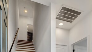A staircase with white walls and a beige floor, leading to a room with a door and a vent on the ceiling. - NEW!  Sleek Rooftop Retreat - Sleeps 10 (Nashville)