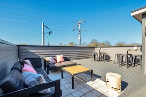 Eine Dachterrasse mit einer Couch, einem Holztisch und Barhocker.