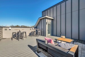 A rooftop terrace with a sofa, bar stools, and a table.
