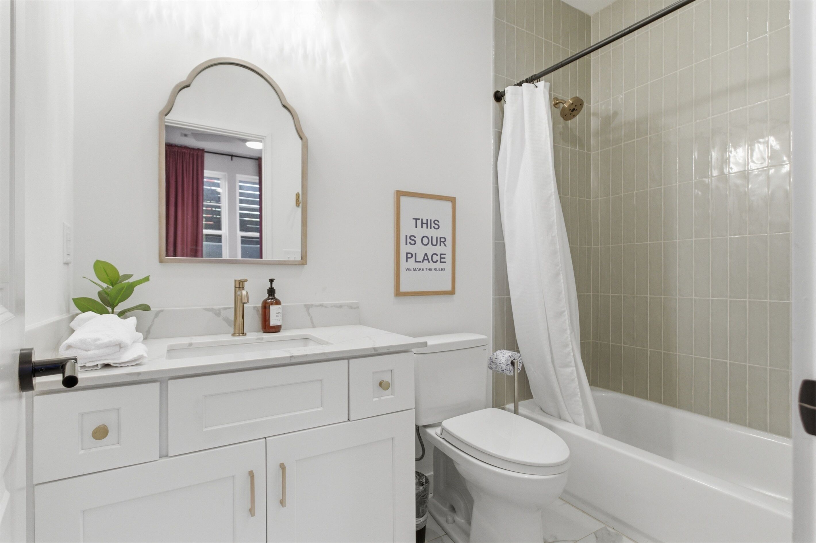 A bathroom with a toilet, sink, mirror, shower curtain, and a framed sign on the wall.
