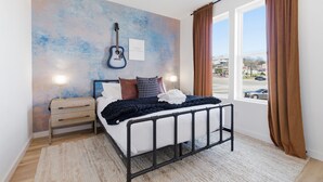 A bedroom with a bed, a guitar on the wall, a nightstand, and a window with curtains.