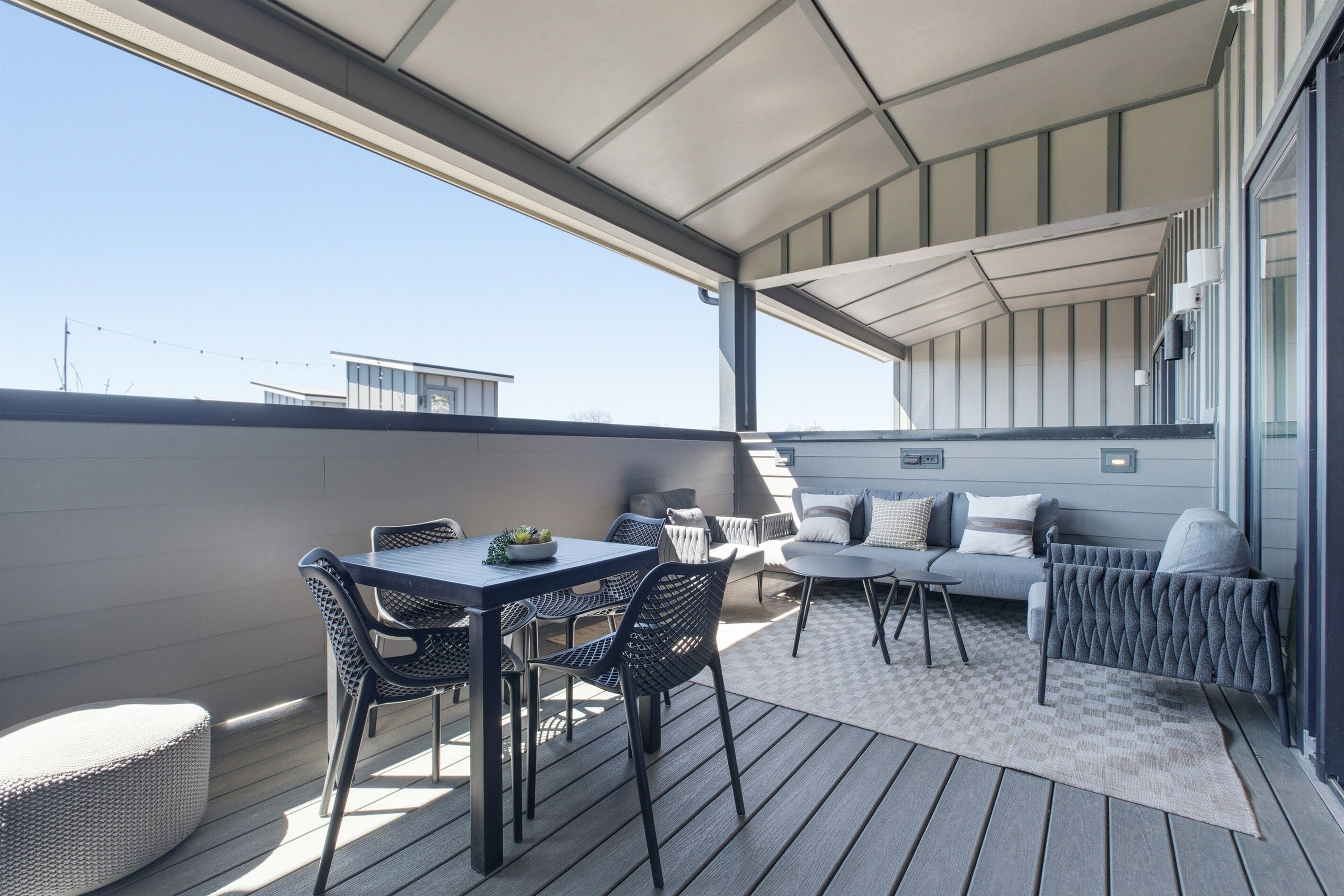 A covered outdoor patio with a table and chairs, a sofa, and a small rug.