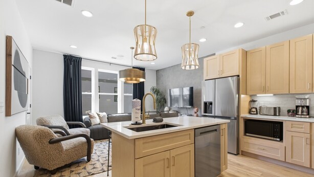 A modern kitchen with wooden cabinets, a central island, stainless steel appliances, and pendant lighting.