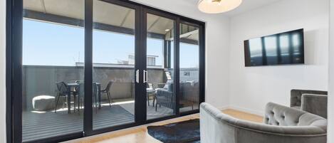 Una sala de estar moderna con un amplio ventanal corredizo que da a un patio exterior, un televisor de pantalla plana en la pared y un sofá capitonado.
