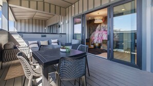 A covered outdoor seating area with a table and chairs, a sofa, and a large sliding glass door leading to an interior space.