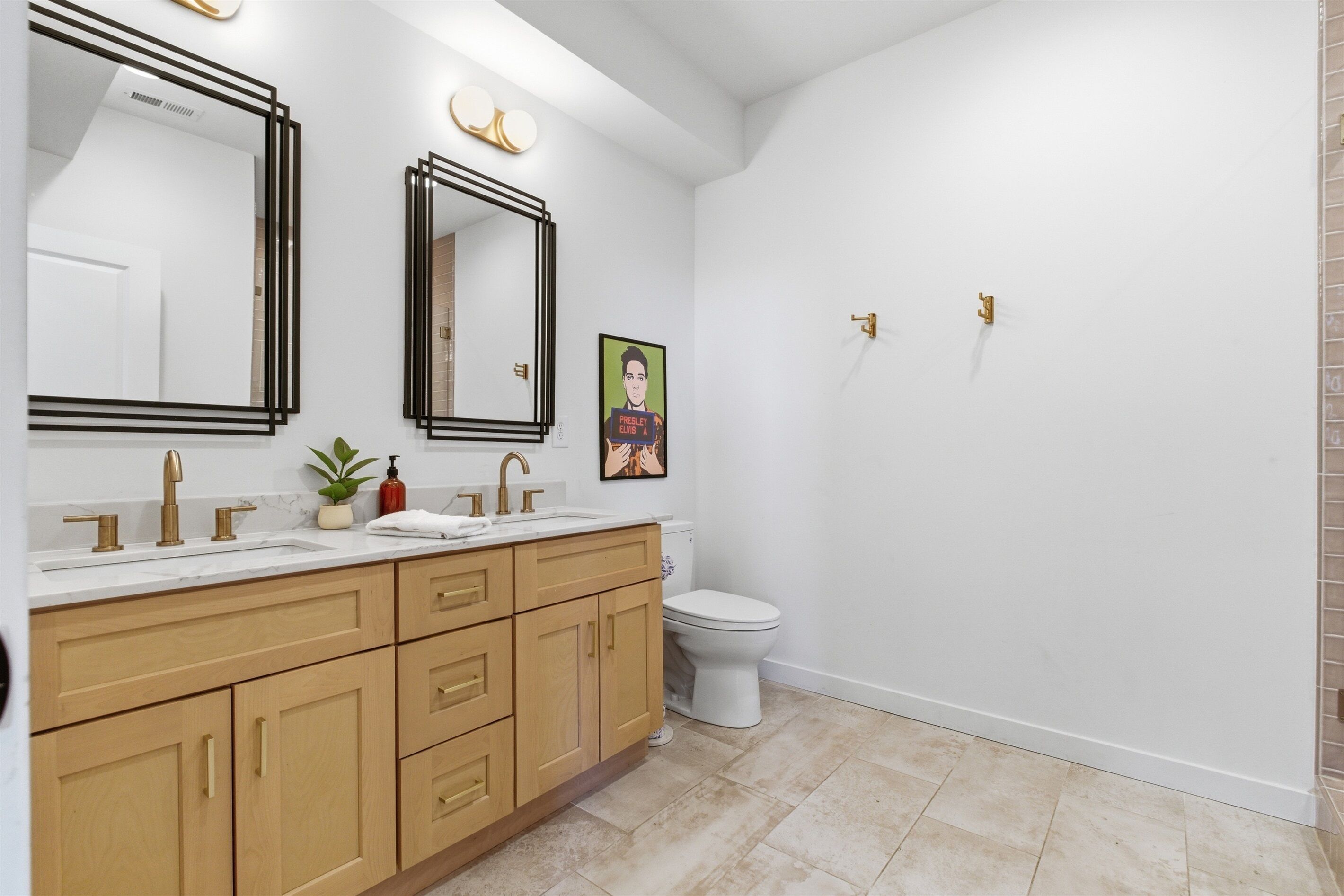 Une salle de bain avec des toilettes blanches, deux miroirs, un lavabo avec un plan de toilette en marbre, des meubles en bois et une petite plante.