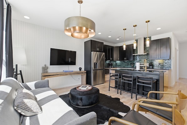 A modern kitchen with a central island, black bar stools, and a flat-screen TV mounted on the wall.