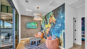 A modern living room with a large mural, comfortable seating, and a television displaying 'IPVanish'. - Rooftop Views + Relaxing Hot Tub & Fire Pit (Nashville)