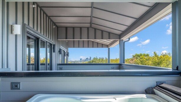 A modern rooftop terrace with a hot tub, large windows, and a city skyline view. - Rooftop Views + Relaxing Hot Tub & Fire Pit (Nashville)