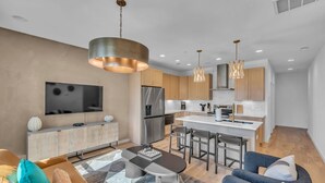A modern kitchen with stainless steel appliances, a dining area with a black table, and a living room with a large TV and comfortable seating. - Rooftop Views + Relaxing Hot Tub & Fire Pit (Nashville)