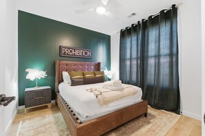 Un dormitorio con cama, mesita de noche, letrero en la pared y ventilador de techo.
