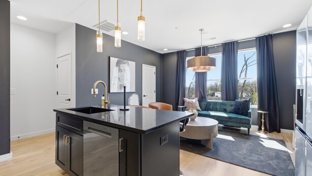 Eine moderne Küche mit Kochinsel, Essbereich mit Sofa und Tisch sowie ein großes Fenster mit Vorhängen.