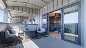 Eine moderne Außenterrasse mit Sitzgelegenheit, eine Glastür zu einem Innenraum mit Wandverkleidung und einem Chandelier.