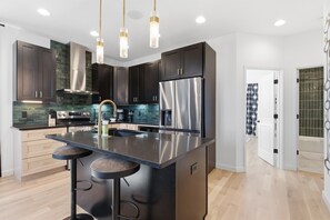 A modern kitchen with dark cabinets, stainless steel appliances, a central island with stools, and pendant lighting.