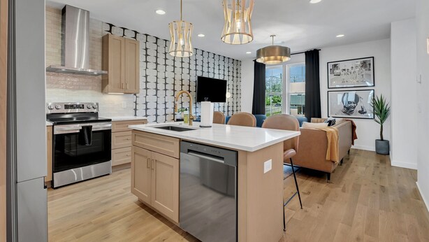 Una cucina moderna con elettrodomestici in acciaio inossidabile, un'isola centrale, luci a sospensione e piastrelle decorative.