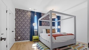 Ein Bett mit Baldachin, ausgestattet mit weißer Bettwäsche, einem farbenfrohen Schachbrettteppich und einer Wand mit Muster.
