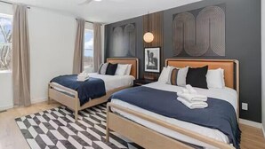 Une chambre d’hôtel moderne avec deux lits, un tapis à motifs géométriques et une grande fenêtre avec des rideaux.