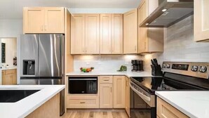 Une cuisine moderne avec des meubles en bois, des appareils en acier inoxydable et un plan de travail blanc.