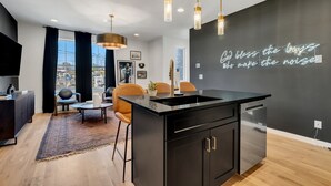 A modern kitchen with a black island, pendant lights, and a neon sign on the wall.
