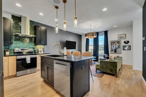 Une cuisine moderne dotée d’un îlot central, d’appareils électroménagers en acier inoxydable et de luminaires suspendus.