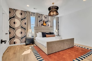 Une chambre avec un grand lit, une guitare et un mur décoré de motifs.