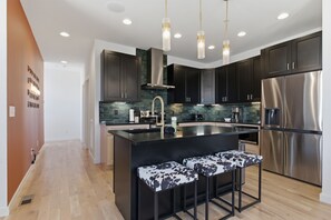 A modern kitchen with dark cabinets, a stainless steel refrigerator, and a central island with bar stools.