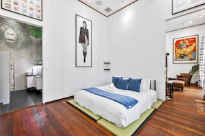 A modern hotel room with a large bed, a bathroom with a glass shower, and a dining area with a table and chairs.