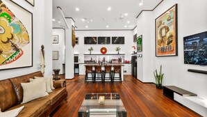 Un salon moderne avec un canapé en cuir marron, une table basse en verre et un coin cuisine doté d’un bar.