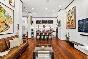 Een moderne woonkamer met een bruine leren bank, een glazen salontafel en een keuken met een bar.
