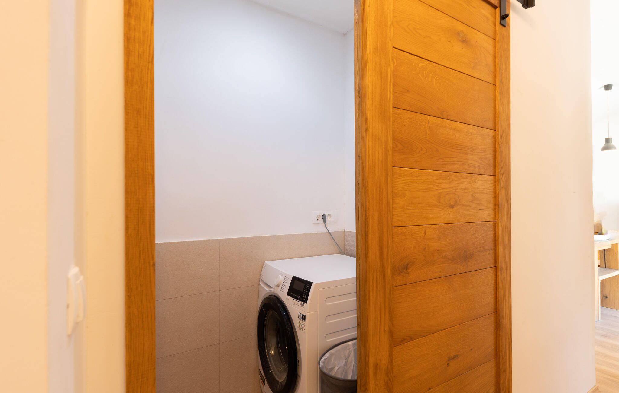 A laundry room with a washing machine and a trash can.
