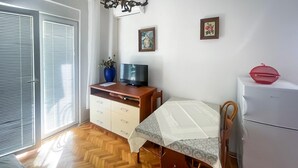 A room with a wooden herringbone floor, a white bed with a patterned bedspread, a small wooden desk with a TV, a white refrigerator, and two framed pictures on the wall. - 1 bedroom awesome apartment in Gradac (Gradac)