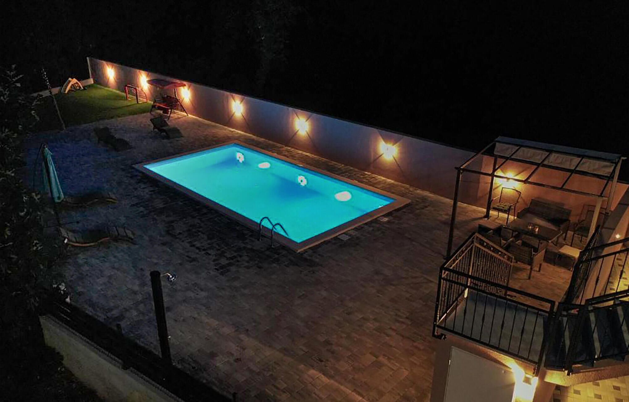 Una piscina con un deck perimetral, un área de descanso cubierta y una escalera que lleva a un nivel superior.