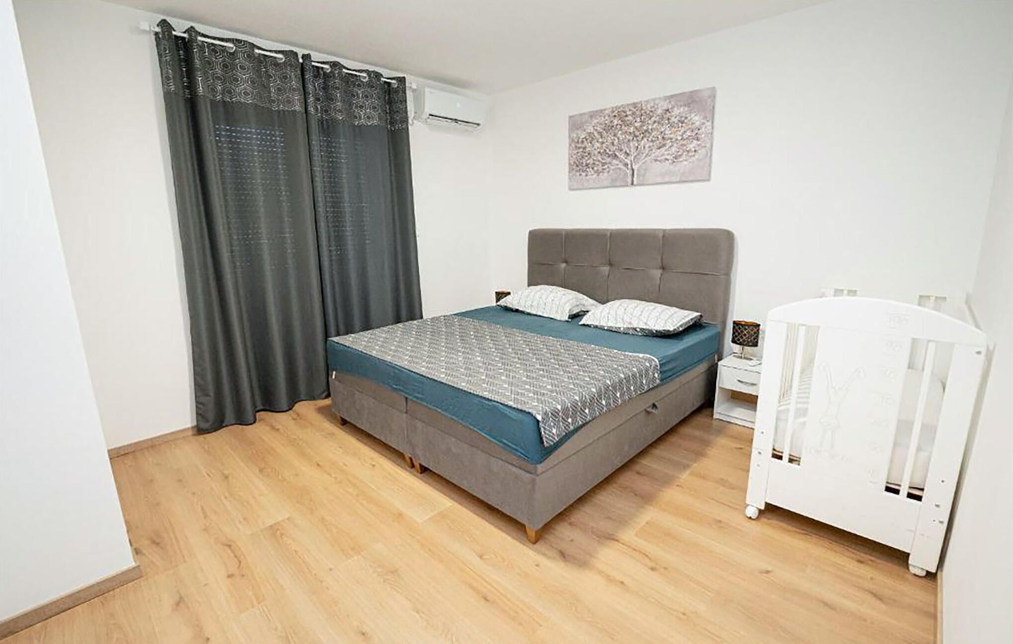 Une chambre à coucher avec un lit, un berceau, un climatiseur fixé au mur et un tableau.