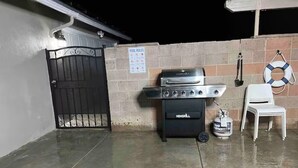 Een terras met een barbecue, een witte stoel en een bord met regels voor het zwembad.