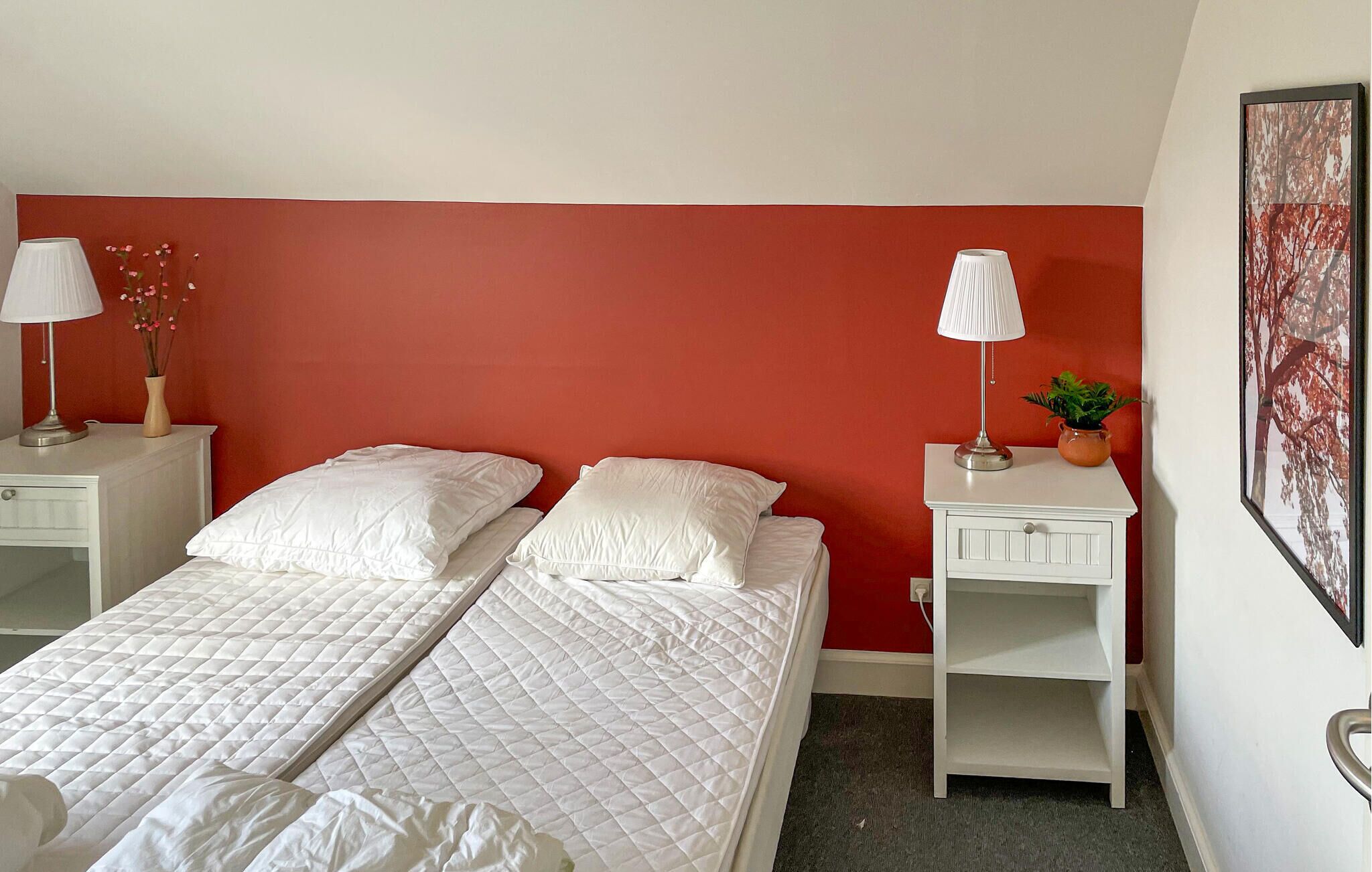 Ett hotellrum med två sängar, vita sängkläder, röda accentväggar, sängbord med lampor, en liten växt och en inramad tavla.