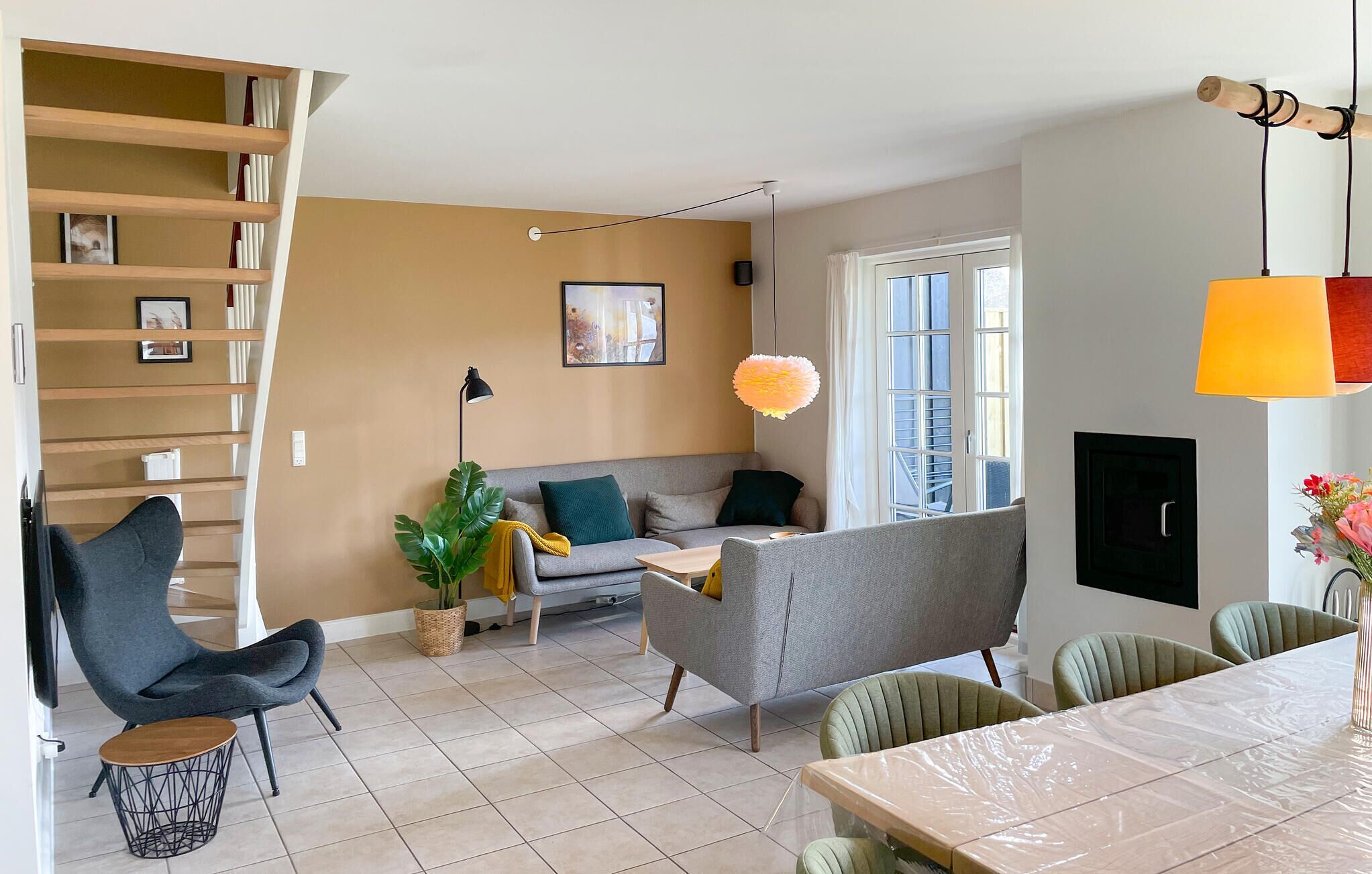 A modern living room with a grey sofa, a dining table, and a staircase with wooden steps.