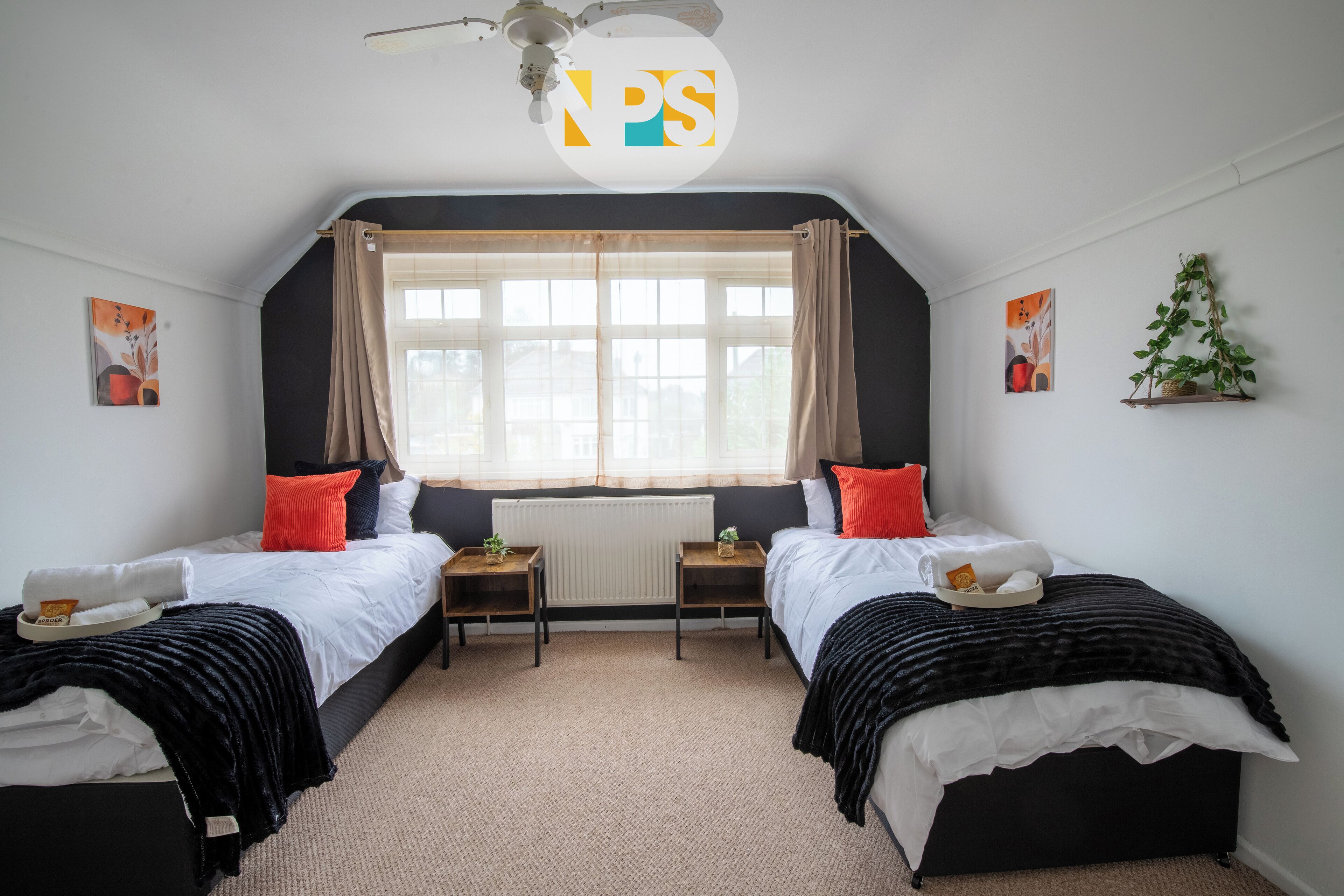 A bedroom with two beds, a window with curtains, a radiator, and artwork on the walls.