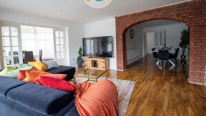 A modern living room with a brick fireplace, a dining area, and a TV. - The Laurels - HS2 Contractors, NEC, BHX Airport Stays, Sleeps 12, Free Parking (Birmingham)