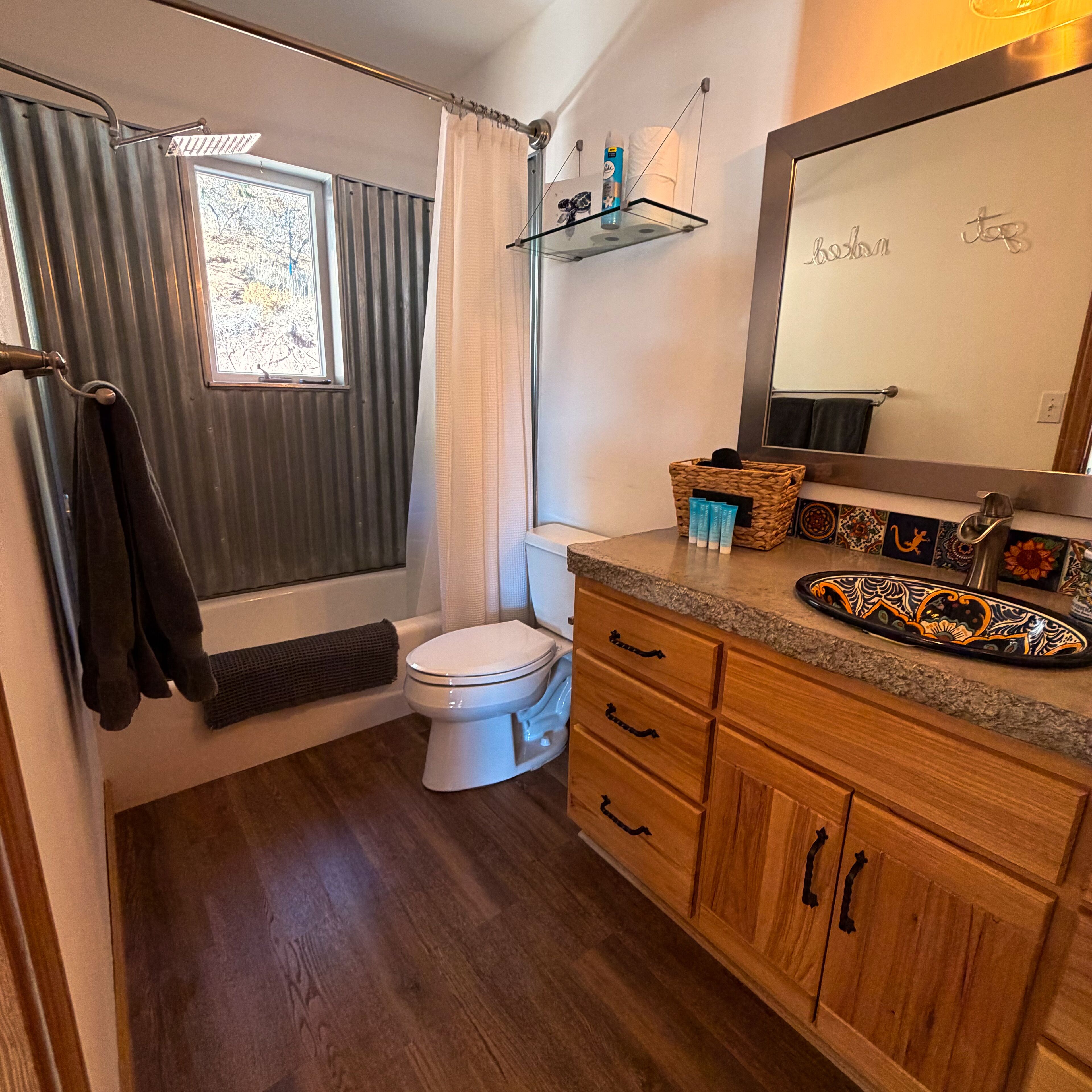 Een badkamer met toilet, douche, wastafel met spiegel en een raam met gordijnen.