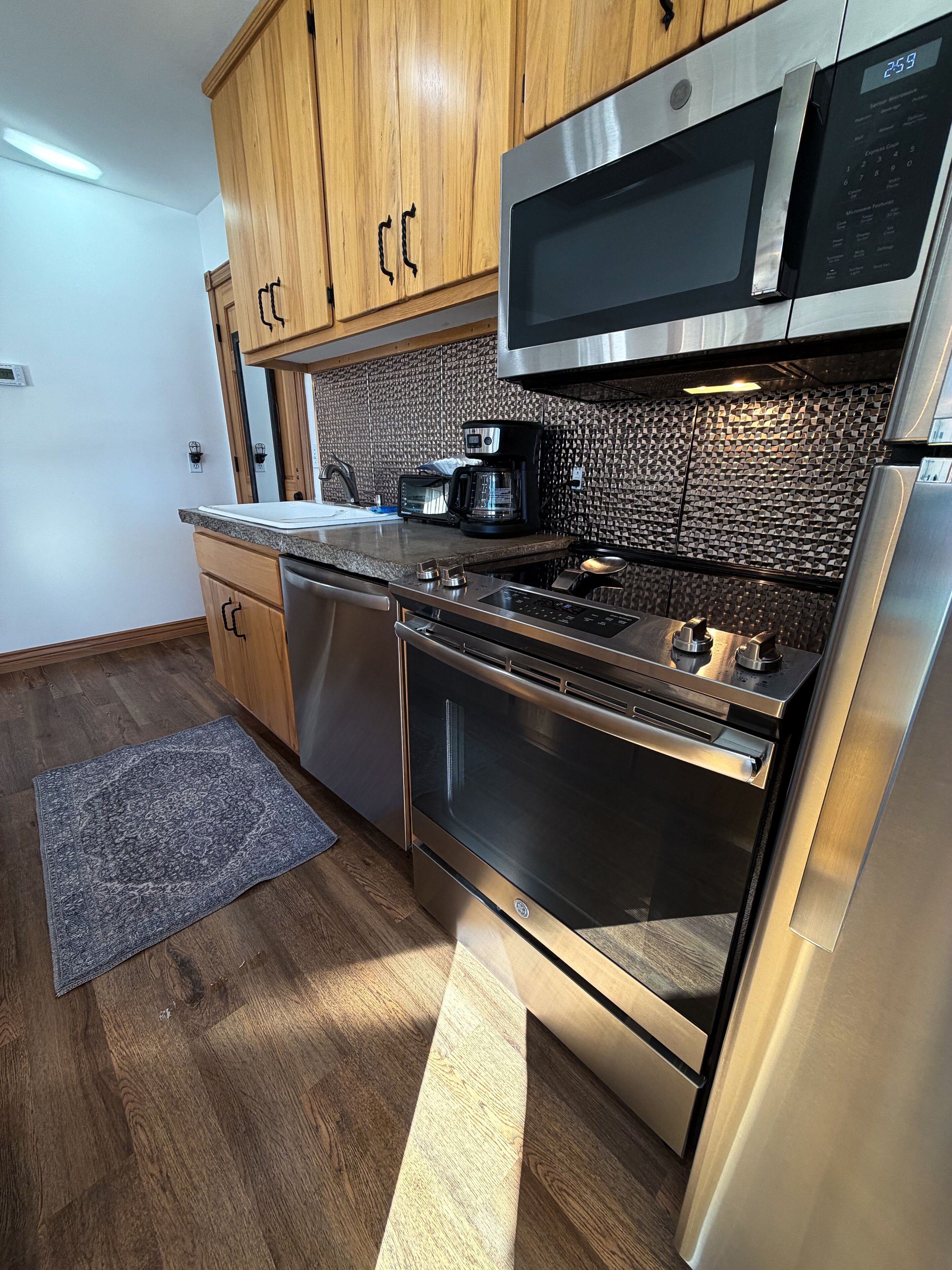 A modern kitchen with stainless steel appliances, wooden cabinets, and a patterned backsplash.