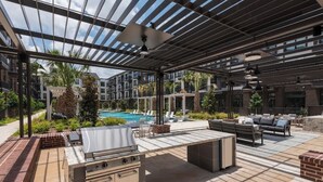 Ein Terrassenbereich im Freien mit Grill, Sitzgelegenheiten und Blick auf einen Swimmingpool.