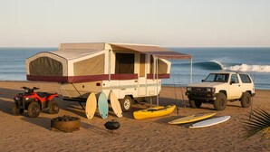 A beach with a camper, ATVs, kayaks, and a truck. - Tranquil RV in San Juanico - 3 Bedrooms (San Juanico)