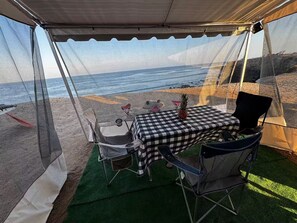 Una carpa junto a la playa con una mesa y sillas a cuadros, una piña y vistas al océano.