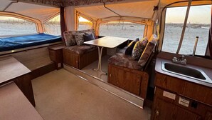 A compact interior with a dining table, cushioned seating, a small kitchenette, and large windows offering a view of the water. - Tranquil RV in San Juanico - 3 Bedrooms (San Juanico)
