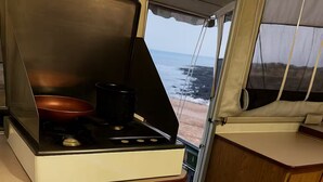 A compact kitchenette with a stove, a small refrigerator, and a view of the beach through a window. - Tranquil RV in San Juanico - 3 Bedrooms (San Juanico)