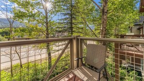 Ein Balkon mit einem Korbstuhl, einem Metallgeländer und Blick auf eine Straße und Bäume.